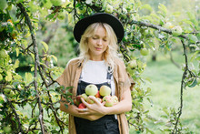 Young Woman Standing In Garden With Apples