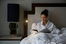 Beautiful young woman reading a book in bed 