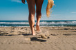 © Patricia Becaroto/ADDICTIVE STOCK - Back view woman cropped legs holding a straw hat walking along coastline in bright sunlight