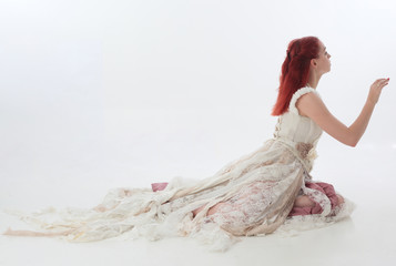 full length portrait of red haired girl wearing torn and tattered wedding dress. Standing pose against a  white studio background.