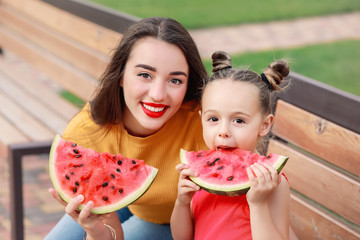 Wall Mural - Cute little girl and her mother eating sweet watermelon in park