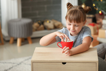 Wall Mural - Cute little girl drinking hot chocolate with marshmallows at home on Christmas eve