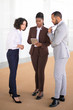 © Mangostar - Young African American manager sharing report details with colleagues. Multiethnic business group standing in hallway, using tablet, discussing issues. Collaboration concept