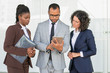 © Mangostar - Serious business group watching presentation on tablet. Multiethnic business man and women standing in hallway, using tablet, looking at screen. Digital technology concept
