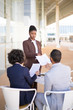 © Mangostar - Serious African American assistant bringing documents to boss and his partner. Business man and woman sitting at table near office building and reviewing contract. Paperwork concept