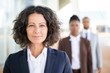 Successful female leader posing with her team in blurred background. Middle aged businesswoman smiling at camera, her two colleagues standing behind her. Successful team leader concept