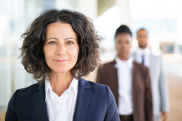 successful female leader posing with her team in blurred background. middle aged businesswoman smili