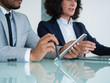 © Mangostar - Professionals using gadgets during conference or corporate meeting. Business man and woman sitting at office table, using computer and tablet. Corporate meeting concept