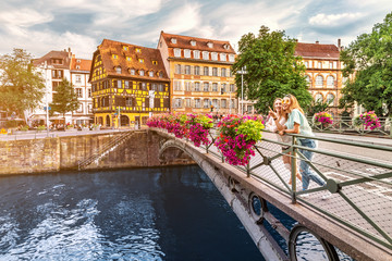 Wall Mural - Two young happy girl friends standing on a bridge in Strasbourg while travelling in Petit France region. Tourism and friendship concept