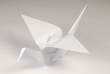 Light Gray Origami Crane On Gray Background. Tsuru. Japanese Art Of Paper Folding. Flat Square Sheet Of Paper Transferred Into Finished Sculpture Through Folding And Sculpting. Close Up. Macro Photo.