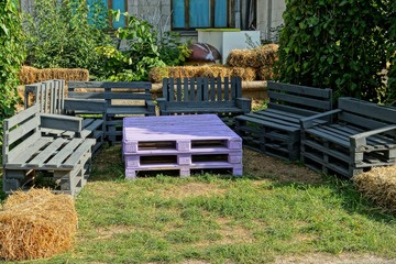 colored table and chairs of wooden pallets stand on the green grass on the street