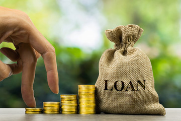 Financial loan agreement concept. A man hand on growth stack of coins and loan bag on wooden table.