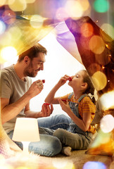 Wall Mural - family, hygge and people concept - happy father and little daughter playing tea party in kids tent at night at home