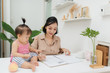 © makistock - Little assistant. Little baby girl using pen while sitting on office desk with her mother in office