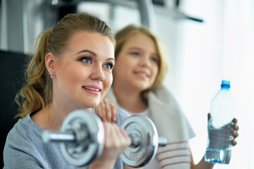 Portrait of sporty young woman and her daughter training with dumbbell in gym