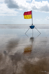 A red and yellow life saving flag against a cloudy blue sky setup by lifeguards in Pendine, Wales