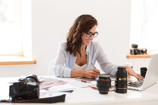Photographer woman in office sit at the table with camera lenses working by laptop computer and graphic tablet.