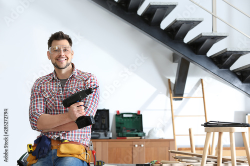 Cuadros en Lienzo Handsome working man with electric screwdriver indoors, space for text