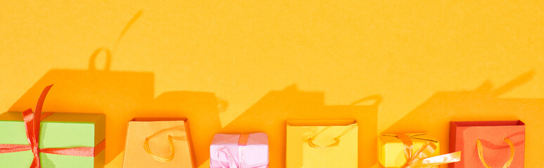 top view of festive wrapped gifts and shopping bags on bright orange background, panoramic shot