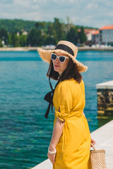 Wall Mural - woman walking by sea quay in summer day in yellow sundress