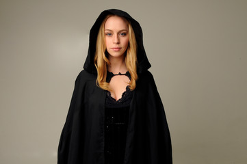 Wall Mural - portrait of blonde woman wearing black hood, halloween witch costume.  creamy studio background.