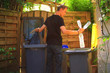 View on profil of one person performing a selective sorting of household waste in recycling bins. Man putting plastic bottles in a yellow container and garbage in a bag in a green container.