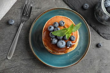 Wall Mural - Tasty pancakes and blueberries served on grey table, flat lay