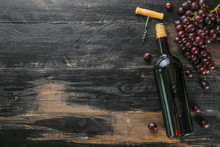 Vintage Bottle Of Red Wine Without Label, Corkscrew & Bunches Of Ripe Organic Grapes On Grunged Wood Table Background. Expensive Bottle Of Cabernet Sauvignon Concept. Copy Space, Top View, Flat Lay.
