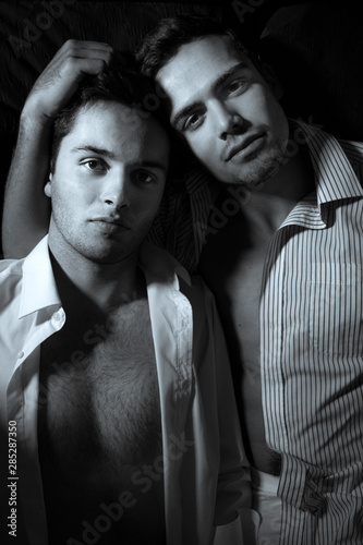 Fototapeta na szkło Gay male couple lying in bed and both looking at the camera