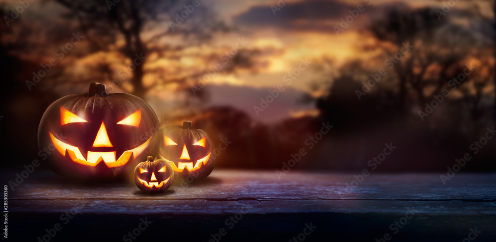 A spooky forest sunset with a haunted evil glowing eyes of Jack O' Lanterns on the left of a wooden bench on a scary halloween night. - obrazy, fototapety, plakaty 