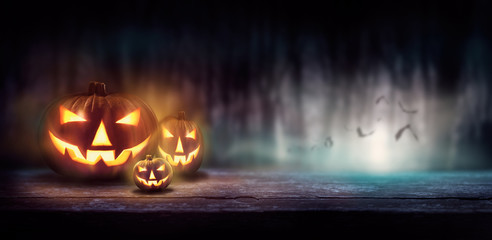 Wall Mural - warm glow of jack o' lanterns on a wood bench in a dark cold forest at night.