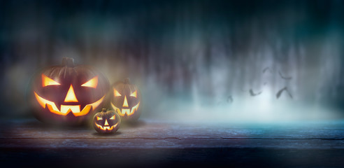 Wall Mural - jack o' lanterns on a wood bench in a cold misty, foggy forest at night with bats in the background.