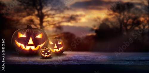 Fotografía A spooky forest sunset with a haunted evil glowing eyes of Jack O' Lanterns on the left of a wooden bench on a scary halloween night