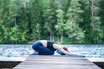 Wall Mural - Young attractive girl practicing yoga, sitting in Child exercise, Balasana pose  on the lake. The concept of appeasement,  healthy lifestyle