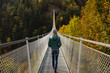 © Michela Ravasio/Stocksy - Woman walking along a suspension bridge