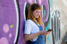 Young Woman Using Smartphone In Front Of Purple Graffiti Wall