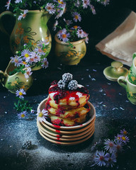 Wall Mural - Cottage cheese pancakes, syrniki, curd fritters with frozen berries (BlackBerry) and powdered sugar in a vintage plate. Gourmet Breakfast. Selective focus, side view with aster flowers vase