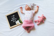 Portrait of sleeping one month old newborn baby girl laying between letter board and teddy bear. Flat lay composition.