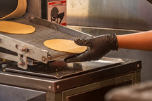 Layers Of Taco Tortilla Shells Coming Out Of A Tortilla Machine While A Hand Grabs A Tortilla In A Mexican Taqueria
