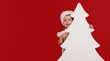 © oes - Happy little girl child in Santa hat peeking from behind blank sign banner in the shape of Christmas trees. Isolated on red background. Space for Your Text. Sale, holidays, christmas, new year concept
