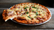 © YUABOG - Homemade pizza with cheese, tomatoes, bacon and herbs in a white ceramic plate on a wooden table.