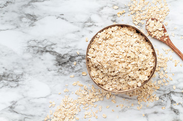 Healthy raw uncooked quick oat flakes in a wooden bowl over a marble table background. Shot from top view.