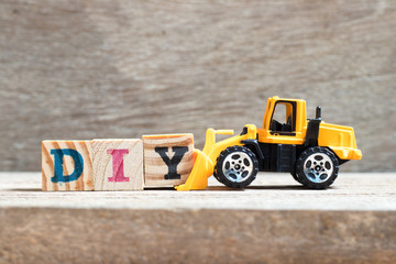 Wall Mural - Toy bulldozer hold letter block Y to complete word DIY (abbreviation of do it yourself)  on wood background