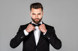 © LIGHTFIELD STUDIOS - elegant smiling man in black suit fixing bow tie isolated on grey