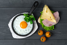 Breakfast Of Fried Eggs And Toast With Cheese, Ham, Lettuce And Cherry Tomatoes On Black Wooden Table. Light Breakfast