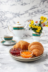 French breakfast with croissants,apricot jam,cherry jam and a cup of tea,red and yellow flowers on white concrete background,close up,space for text,Valentine`s Day breakfast