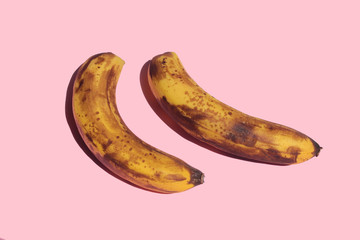 Two overripe bananas on a pink background