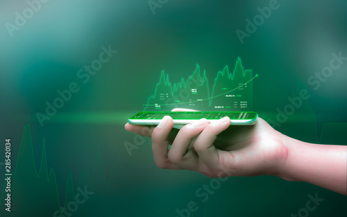 Fotomural Businessman holding smartphone and showing holographic graphs and stock market statistics gain profits