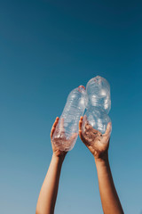 female hands holding two empty plastic transparent water without cap against the sky - environmental