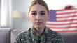 Sad female soldier in camouflage uniform looking at camera, USA flag background